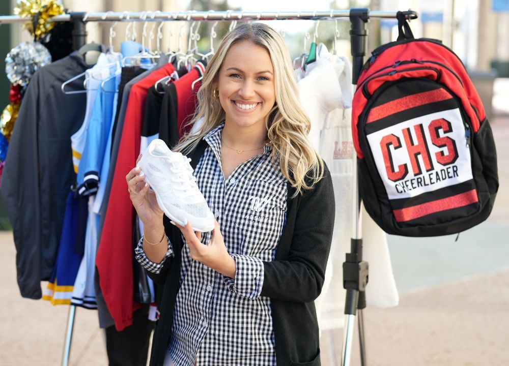 varsity spirit fashion rep holding cheer shoe standing in front of a rack of varsity cheer uniforms